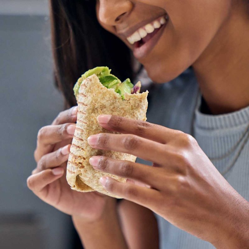 smiling-woman-eating-a-delicious-healthy-wrap-2026-03-25-07-01-47-utc